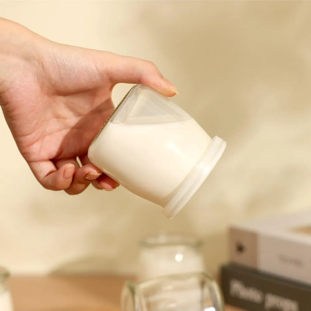 A hand holding an individual glass yogurt vessel filled with yogurt